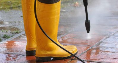 person-wearing-yeallow-rubber-boots-with-high-pressure-water-nozzle-cleaning-dirt-tiles_11zon